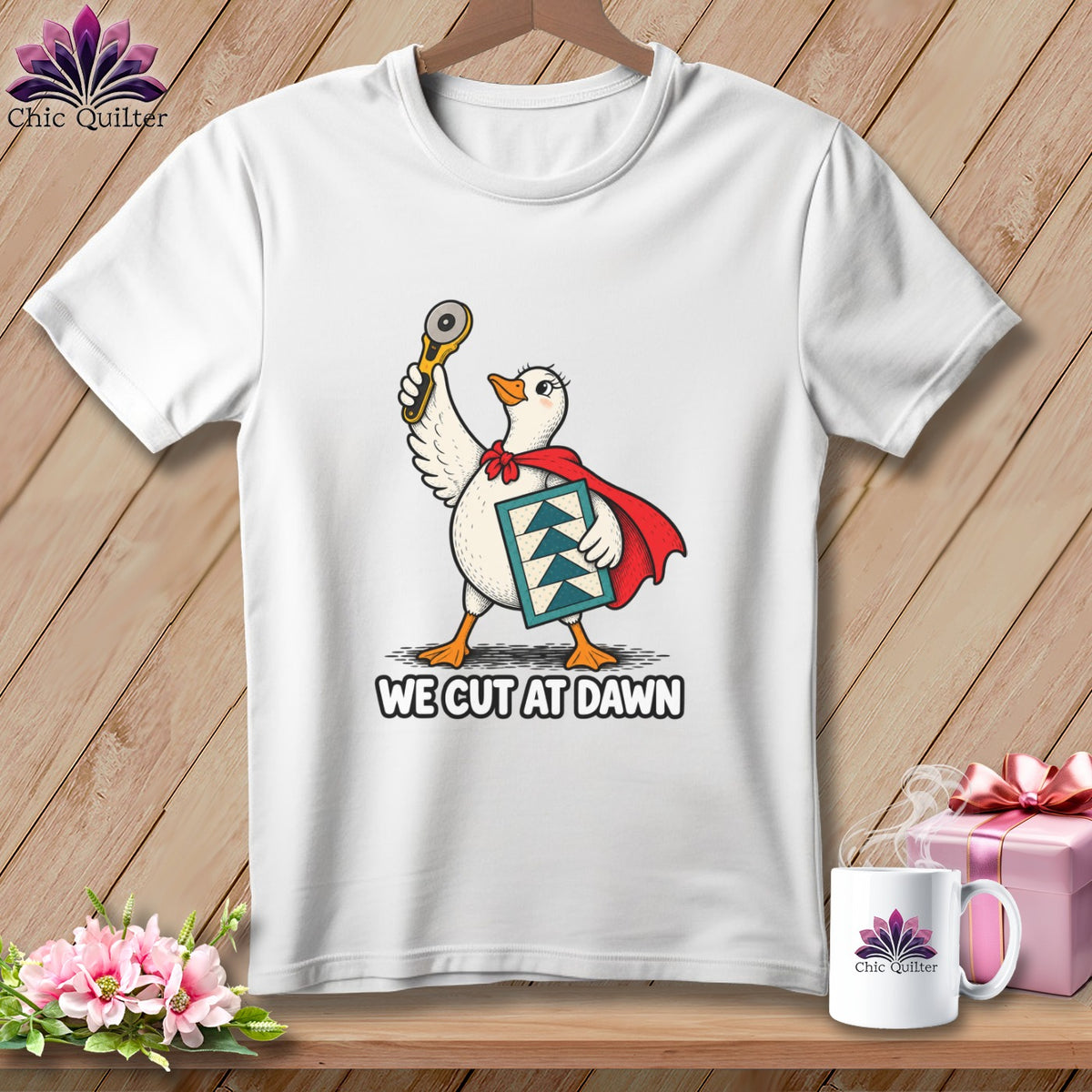 White t-shirt featuring a cartoon duck in a red cape holding a rotary cutter with text We Cut At Dawn.