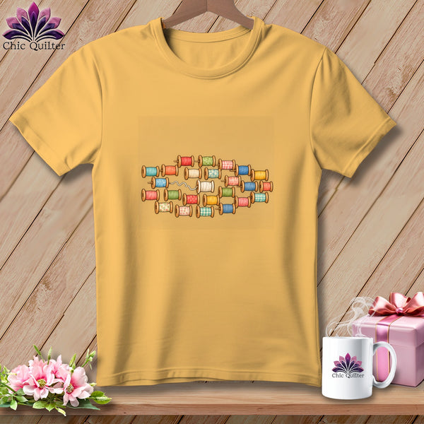 Gold crewneck t-shirt featuring a centered graphic of colorful wooden thread spools.