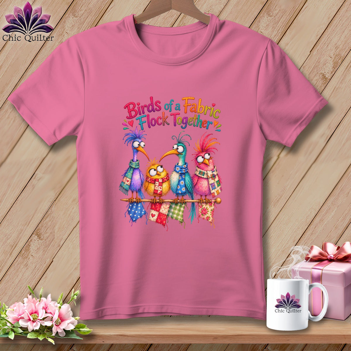 Pink t-shirt with a graphic of four colorful cartoon birds wearing scarves, and text that reads "Birds of a Fabric Flock Together".