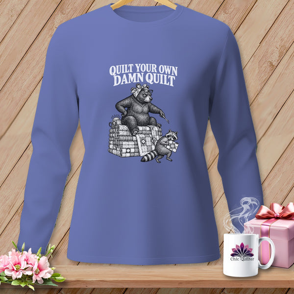 Periwinkle long-sleeve shirt with a vintage graphic of a bear and raccoon quilting and the text Quilt Your Own Damn Quilt.