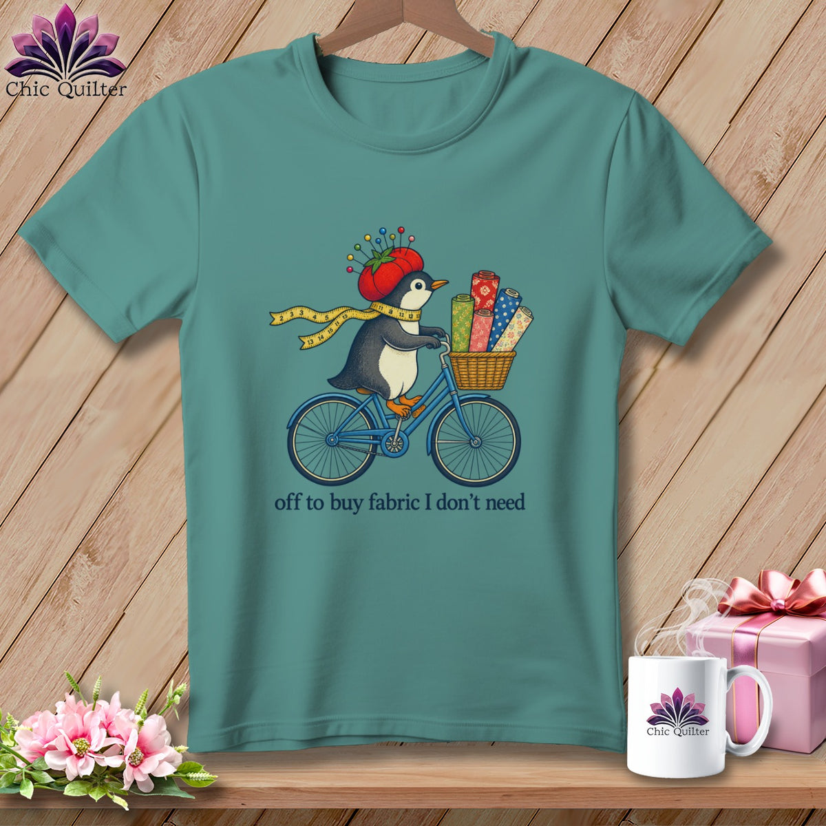 Teal t-shirt with penguin on a bicycle carrying fabric rolls and the text "off to buy fabric I don't need".