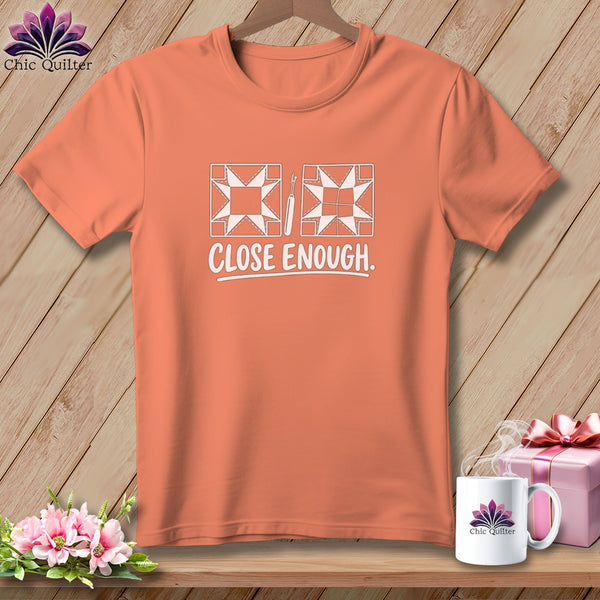 Peach t-shirt with white graphic of quilt blocks, a seam ripper, and text "CLOSE ENOUGH."