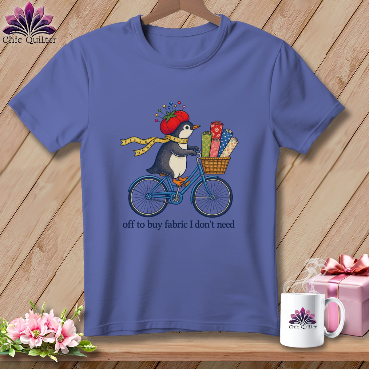 Penguin on a bicycle with fabric rolls and the text "off to buy fabric I don't need".