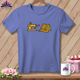 Purple t-shirt featuring a yellow sewing machine and quilt graphic hanging on a wooden wall.
