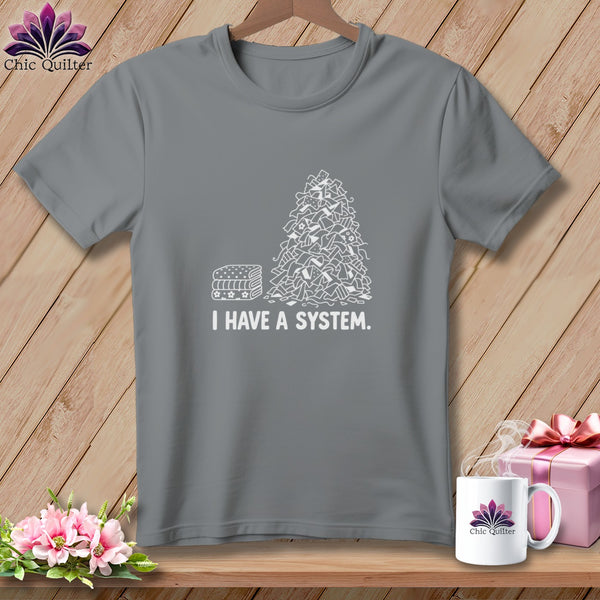 Grey t-shirt with a pile of fabric scraps and "I HAVE A SYSTEM." text.