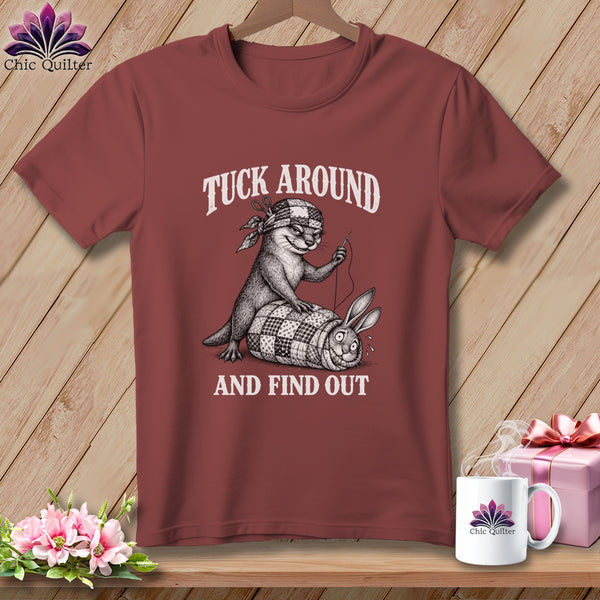 Maroon t-shirt featuring a graphic of an otter sewing a rabbit into a quilt, with text reading TUCK AROUND AND FIND OUT.