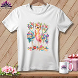 A white t-shirt featuring a colorful illustration of three cute birds wearing glasses and flower crowns while sewing.