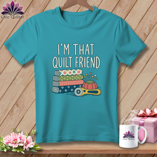 Teal crewneck t-shirt featuring the text I'M THAT QUILT FRIEND above stacked fabric rolls, a pincushion, and a rotary cutter.
