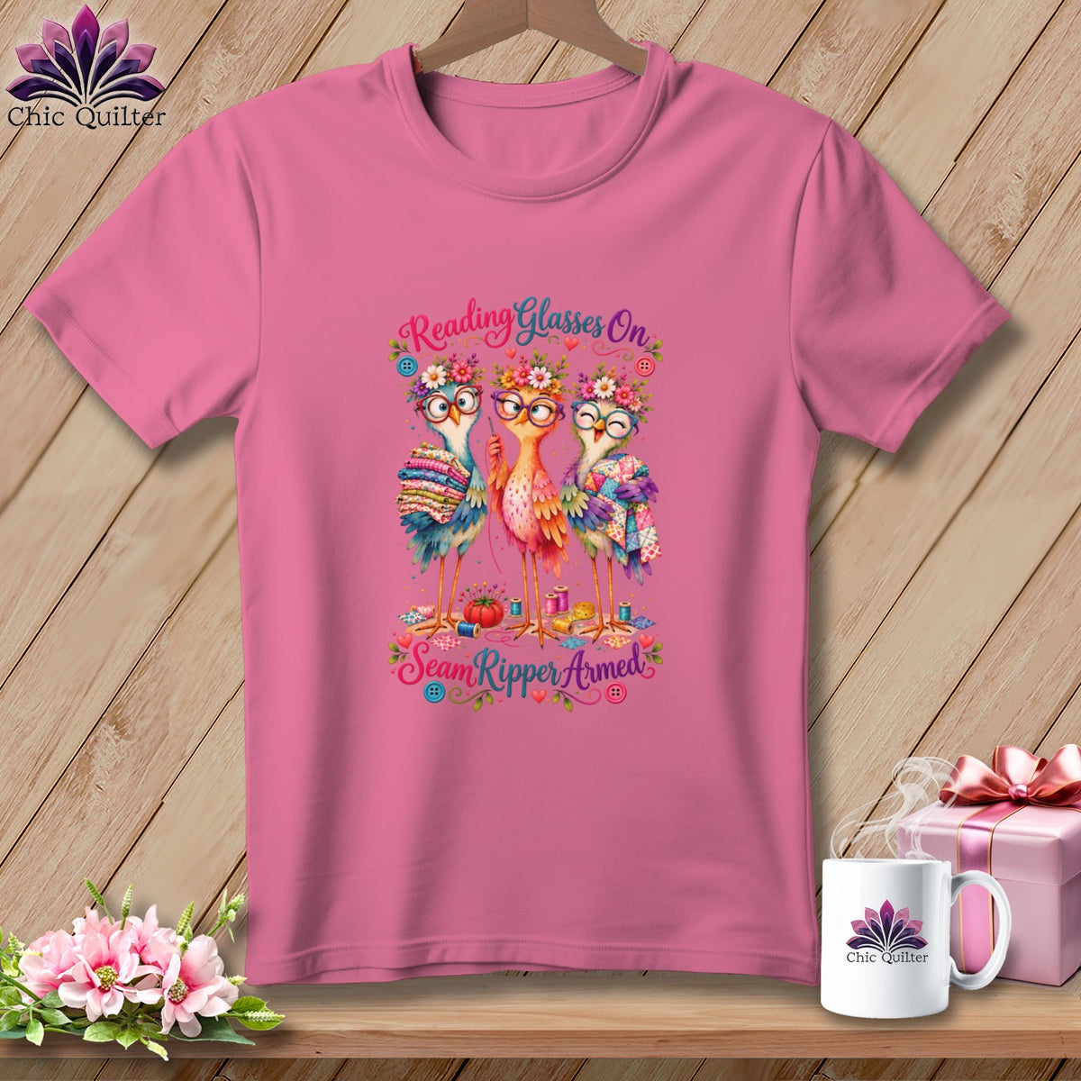 Pink t-shirt with a graphic of three cute birds wearing glasses and flower crowns, holding quilting supplies.