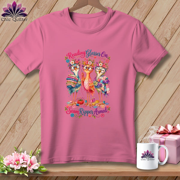 Pink t-shirt with a graphic of three cute birds wearing glasses and flower crowns, holding quilting supplies.
