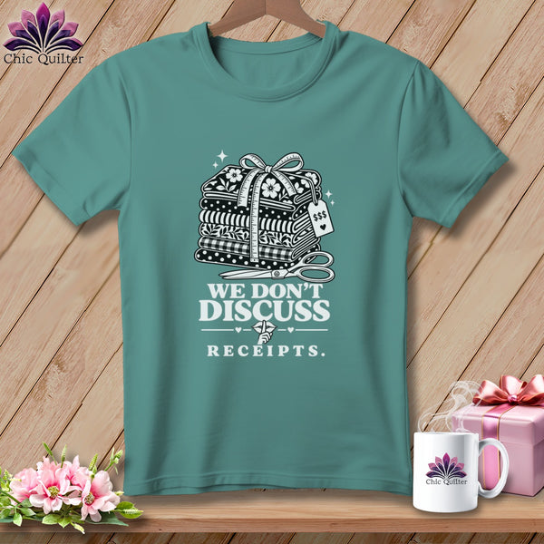 T-shirt with stacked fabric bundles, scissors, and text "We Don't Discuss Receipts."