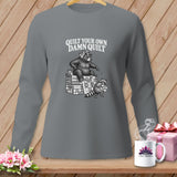 A gray long-sleeve shirt with a graphic of a bear sitting on folded quilts, with text reading 