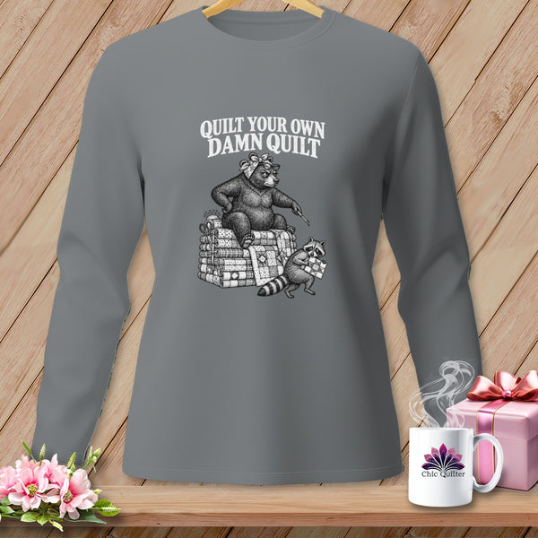 A gray long-sleeve shirt with a graphic of a bear sitting on folded quilts, with text reading "QUILT YOUR OWN DAMN QUILT."