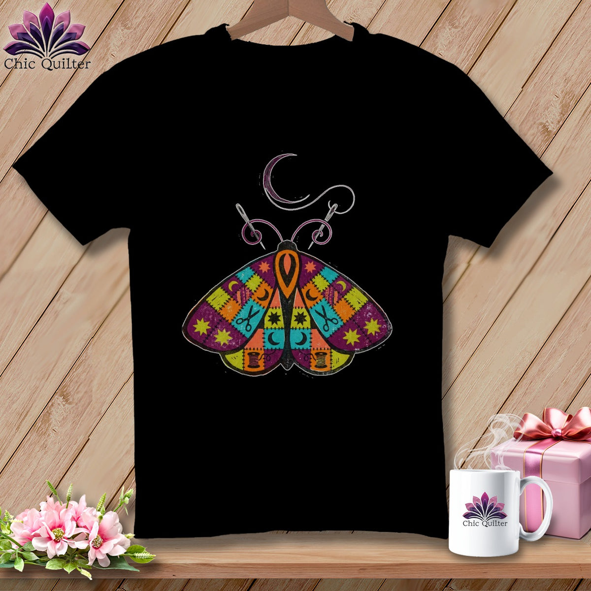 Black t-shirt with a colorful patchwork moth design featuring sewing tools.