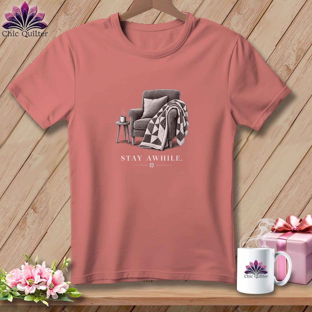 Pink t-shirt with sketch of armchair, quilt, and mug with text "STAY AWHILE."