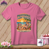 Pink t-shirt with graphic of a woman relaxing on a beach beside a stack of folded fabrics.