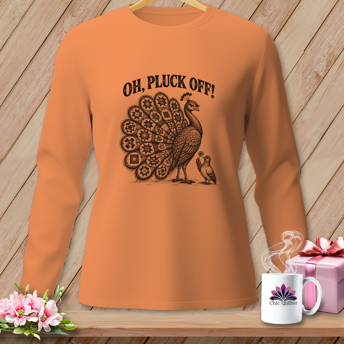 Orange long-sleeve shirt with a vintage peacock graphic and the text OH, PLUCK OFF! on a wooden background.