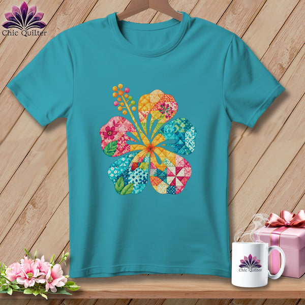 Teal t-shirt featuring a colorful patchwork hibiscus flower graphic on a wooden background with accessories.