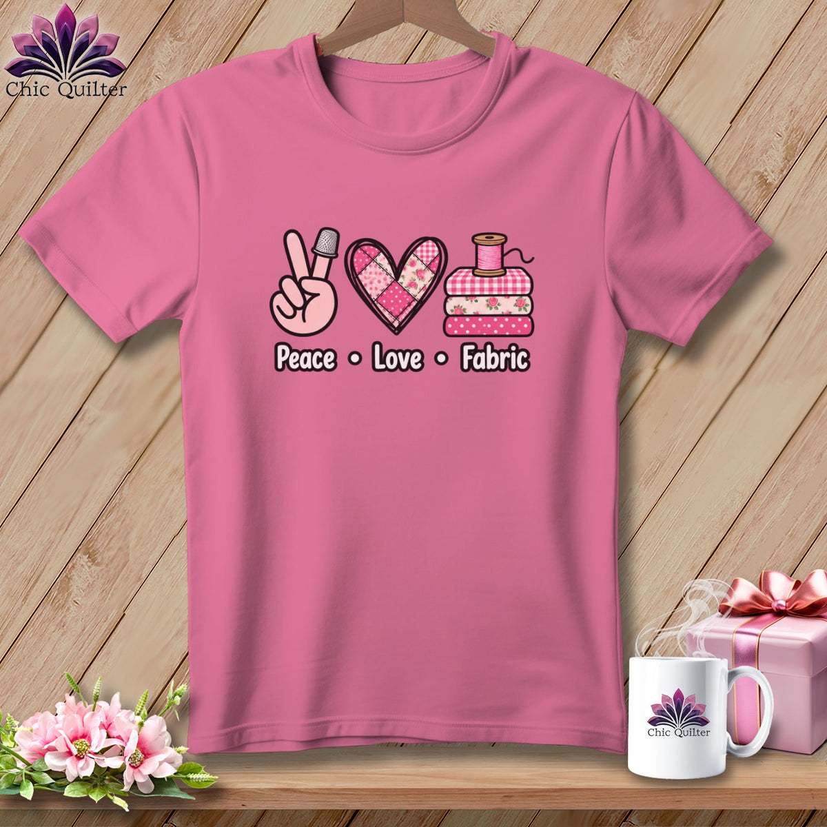Pink t-shirt featuring a quilting graphic with peace sign, patchwork heart, and folded fabrics above the text Peace Love Fabric.