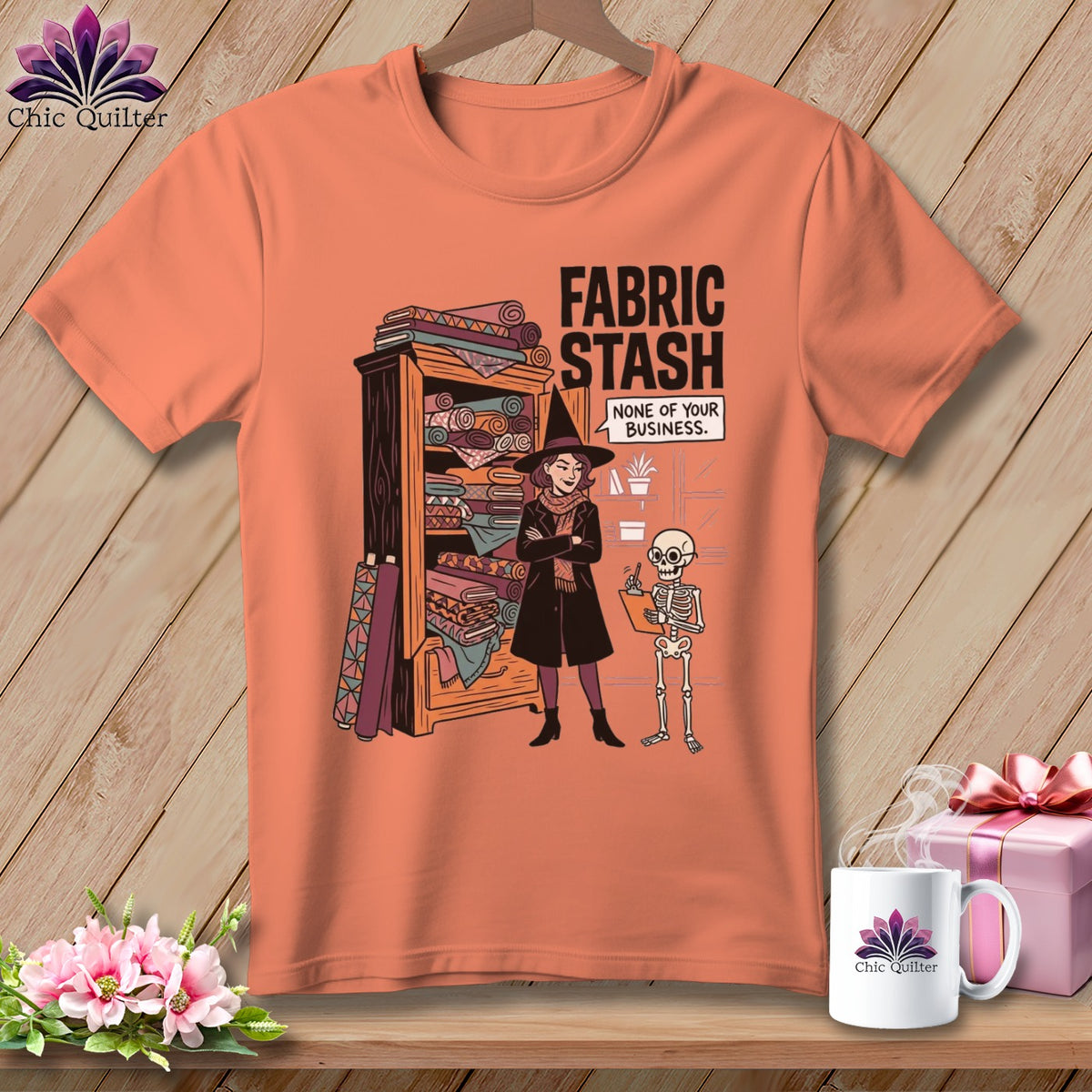 T-shirt graphic with witch and skeleton by fabric shelves, "FABRIC STASH" text.