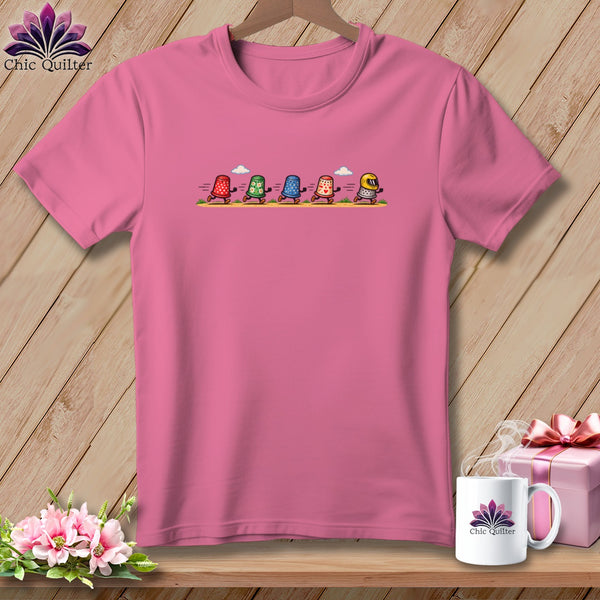 Pink crew neck t-shirt featuring a graphic of five running thimbles on a wooden background.