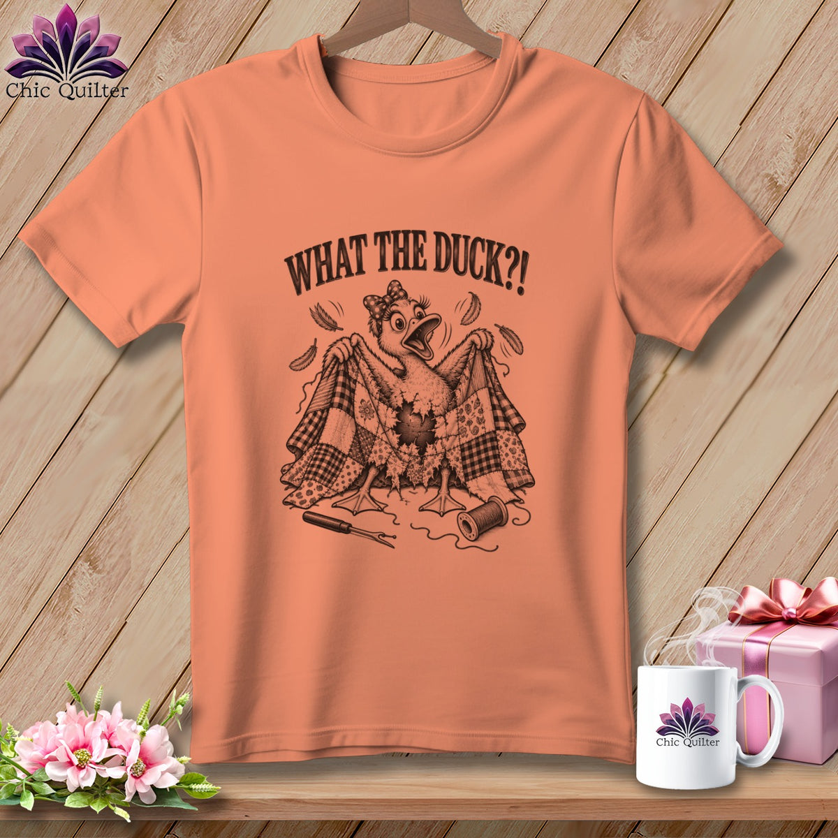 Peach t-shirt with a humorous graphic of a duck ripping a quilt, text WHAT THE DUCK?!, and sewing supplies.