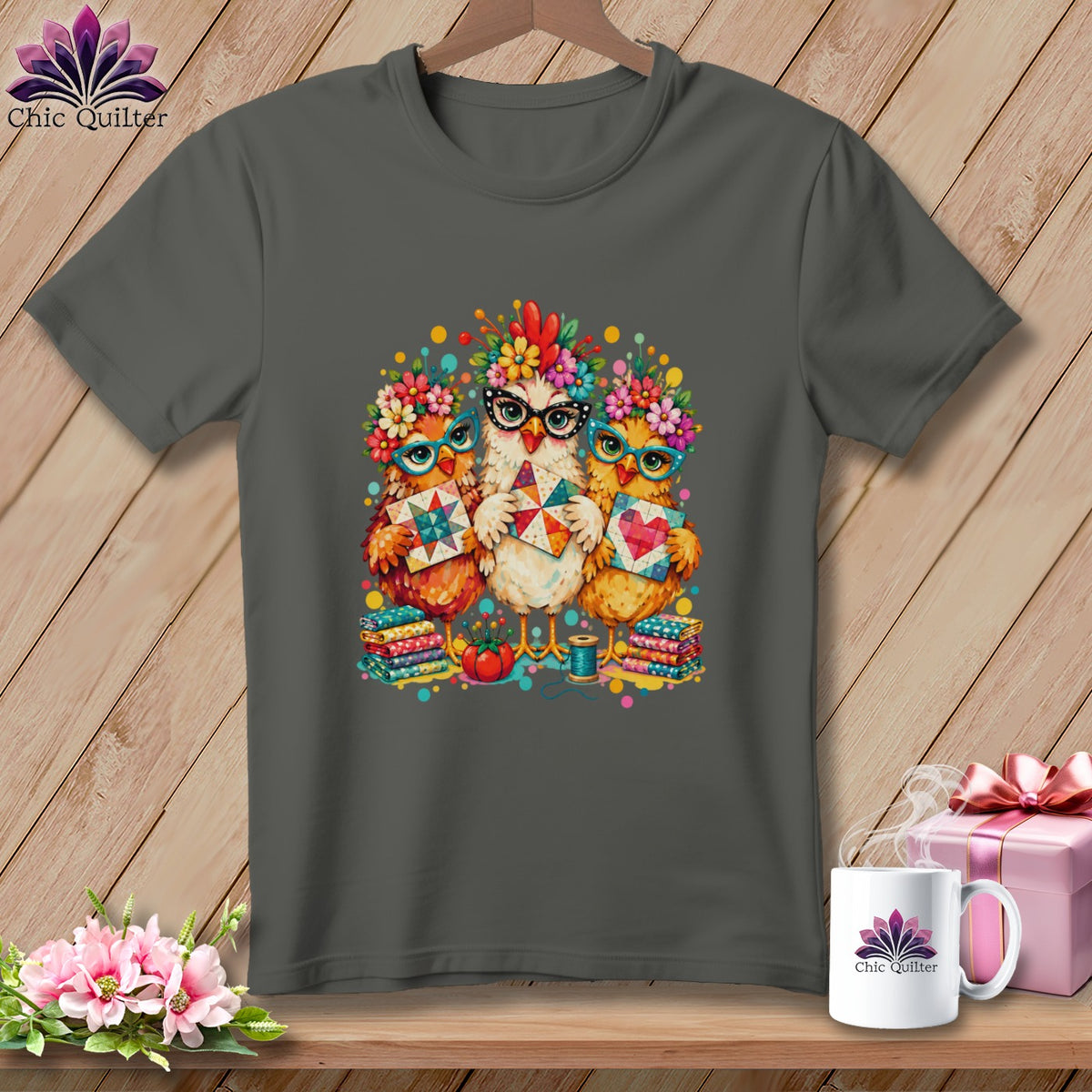 A dark gray t-shirt featuring a colorful graphic of three chickens wearing glasses and floral crowns while holding quilt blocks.