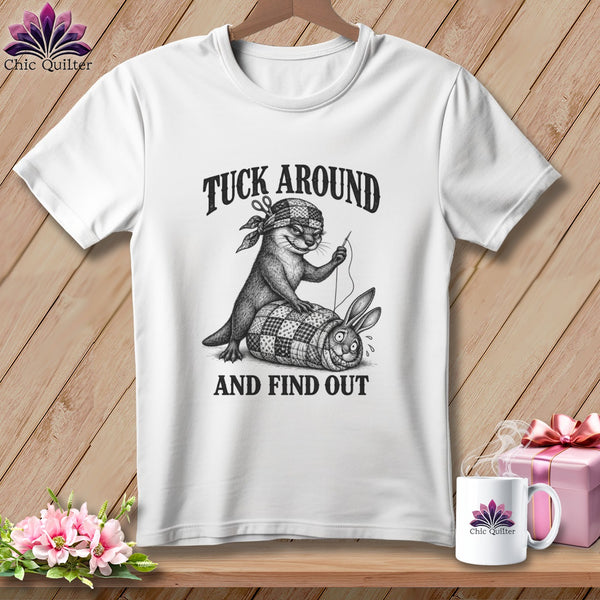 A white t-shirt featuring a black graphic of an otter sewing a rabbit into a quilt, with text reading "TUCK AROUND AND FIND OUT."
