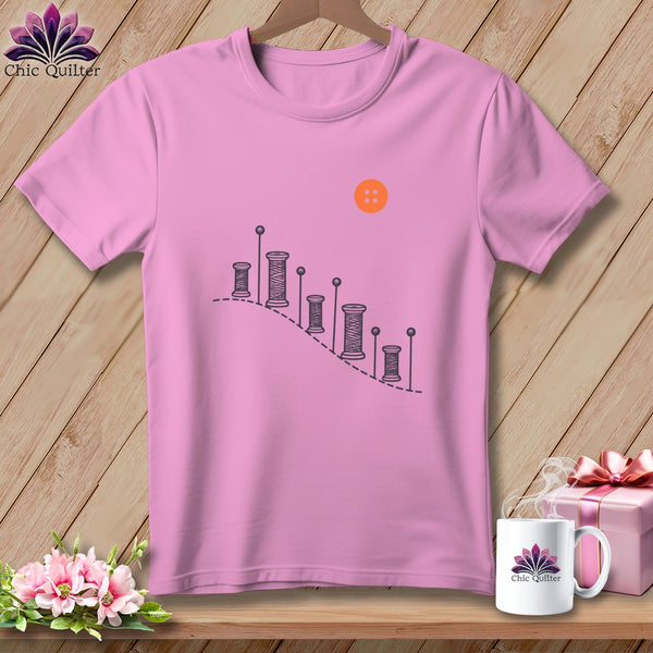 Pink t-shirt with sewing spool graphic and orange button detail.