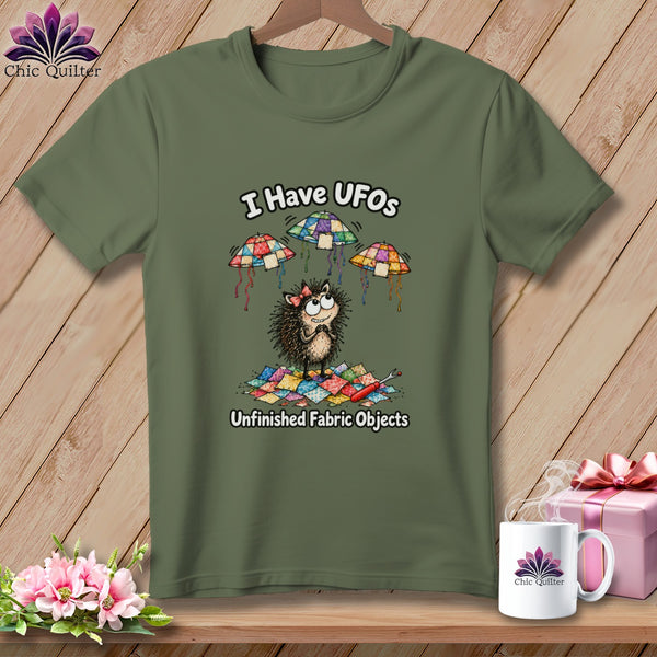 An olive-green t-shirt featuring a cartoon hedgehog with the text I Have UFOs Unfinished Fabric Objects.