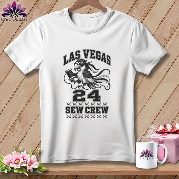 A white t-shirt features a graphic with a parrot holding a spool of thread, text reading Las Vegas 24 Sew Crew, and decorative scissors.