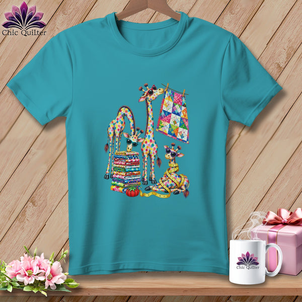 Teal crewneck t-shirt featuring a colorful graphic of giraffes sewing and stacking vibrant quilts.