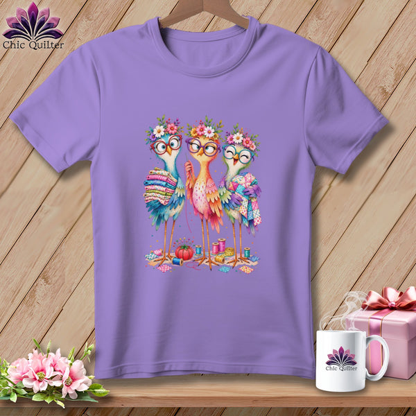 A light purple t-shirt displays a graphic of three colorful birds wearing glasses and flower crowns.