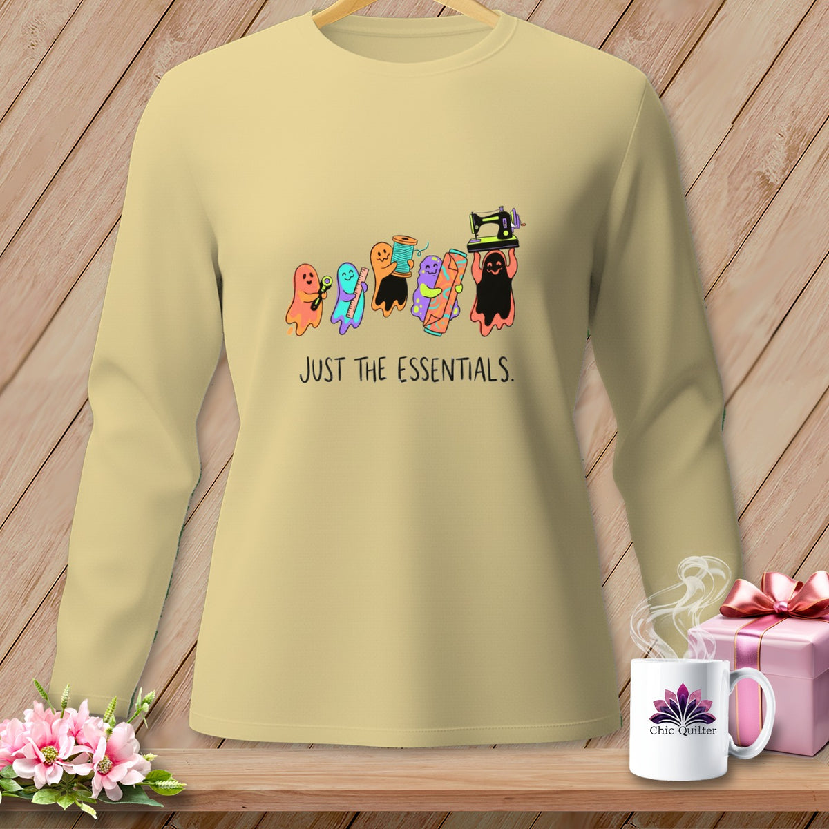 Light yellow sweatshirt with colorful ghosts holding sewing supplies and text "JUST THE ESSENTIALS."