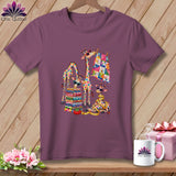 A purple t-shirt hangs on a wooden hanger, featuring a colorful graphic of giraffes with quilting supplies.