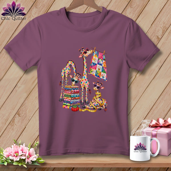 A purple t-shirt hangs on a wooden hanger, featuring a colorful graphic of giraffes with quilting supplies.