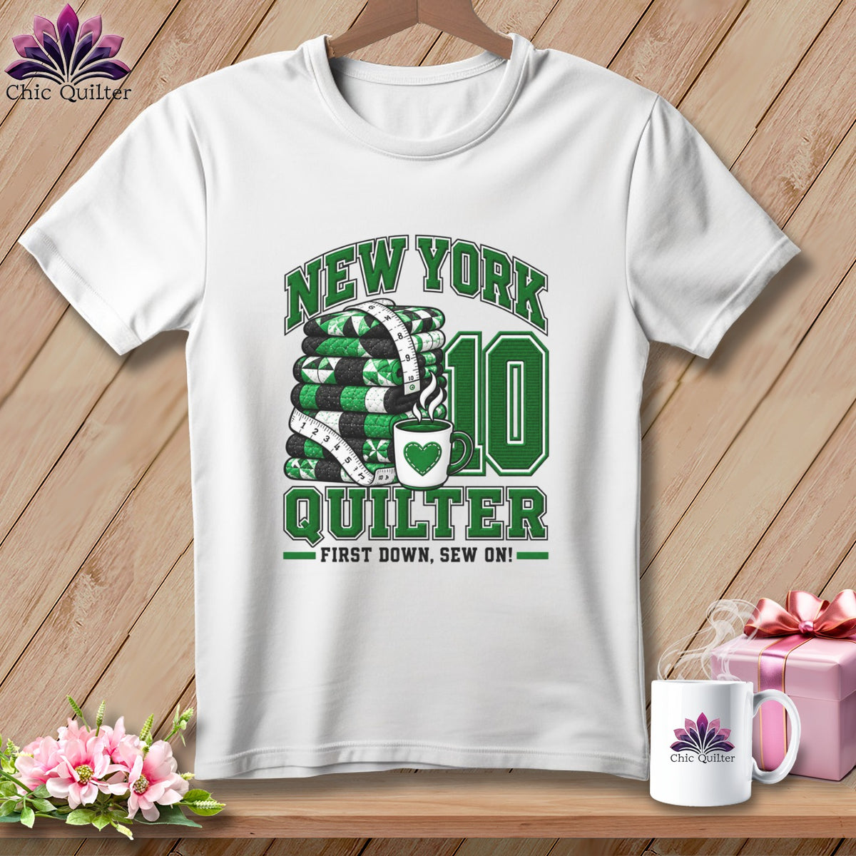 A white crewneck t-shirt featuring green quilting-themed text and graphics on a wooden background.