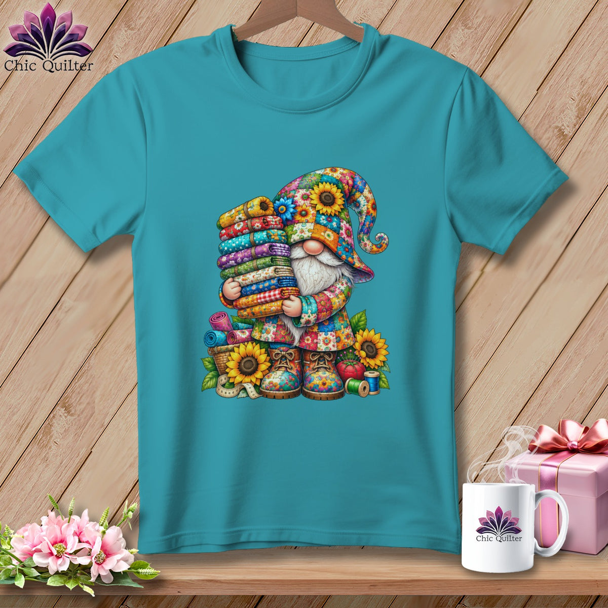 Teal short-sleeved t-shirt featuring a colorful floral gnome holding a stack of fabric rolls.