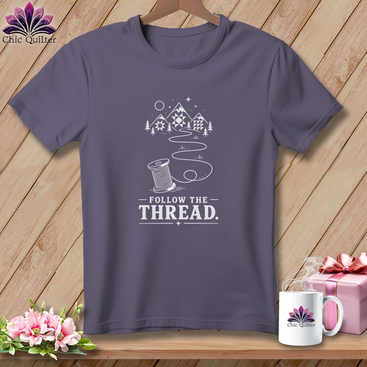 Purple t-shirt with a spool of thread, mountains, and "Follow the Thread." text.