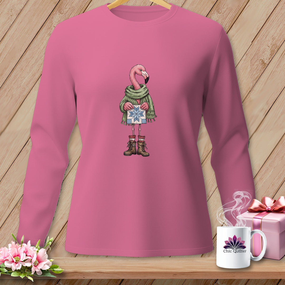 Pink long-sleeve shirt with a flamingo wearing a scarf and boots holding a gift.