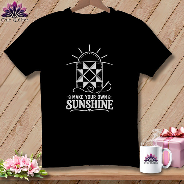 Black t-shirt with white graphic of a quilt square, sun, and needle, reading "MAKE YOUR OWN SUNSHINE".