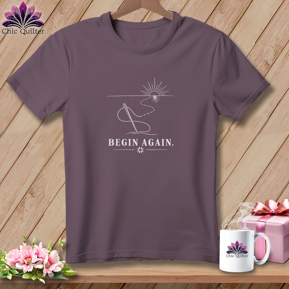 Purple t-shirt with sewing needle, thread, sunrise, and "BEGIN AGAIN." text.