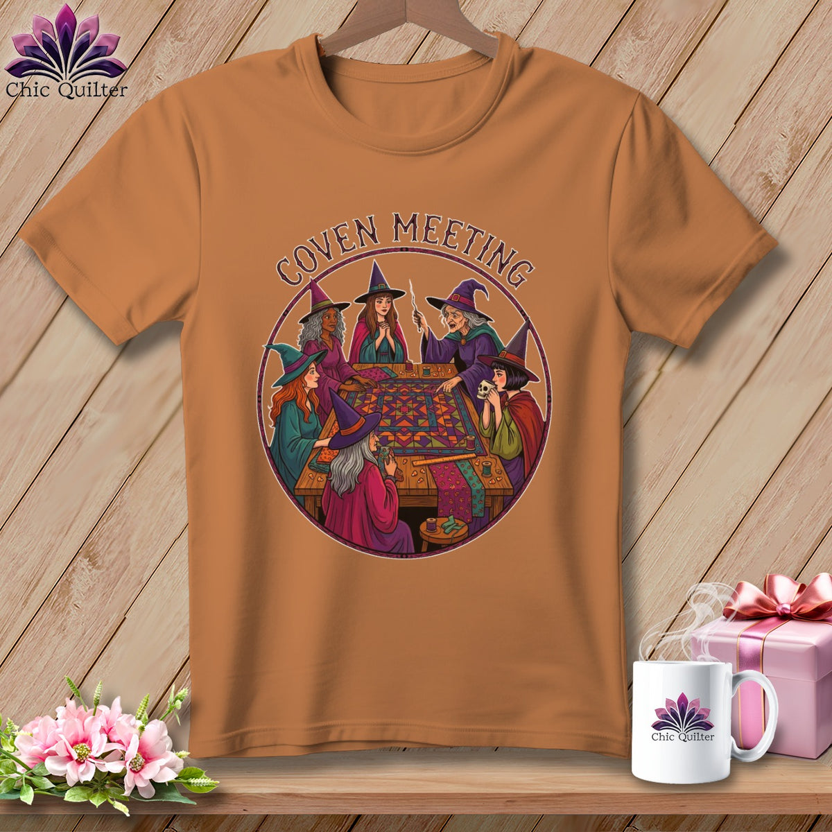 T-shirt graphic of witches gathered around a quilt frame with text "Coven Meeting".