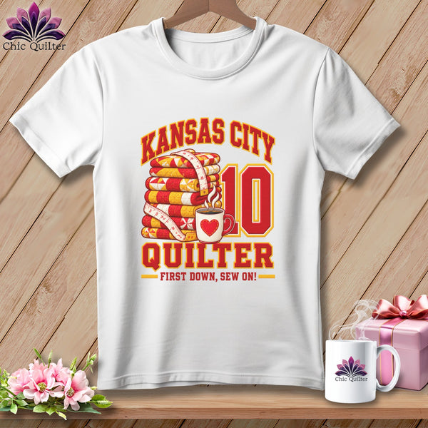 White t-shirt featuring a Kansas City Quilter design with a stack of quilts, coffee mug, and number 10.