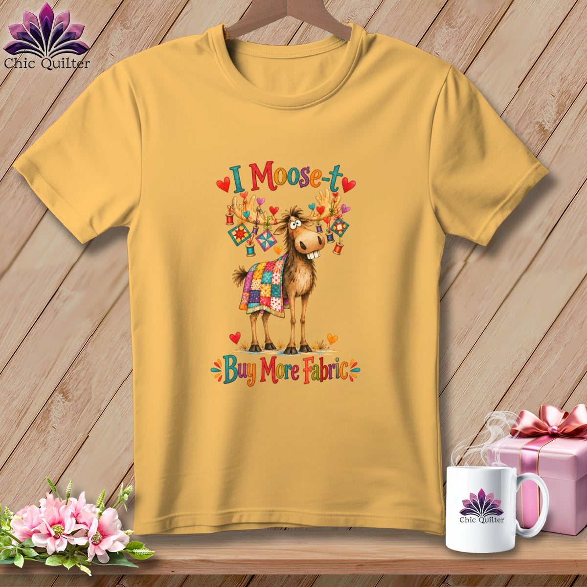 Yellow t-shirt printed with a cartoon moose draped in a quilt, accompanied by the text "I Moose-t Buy More Fabric".