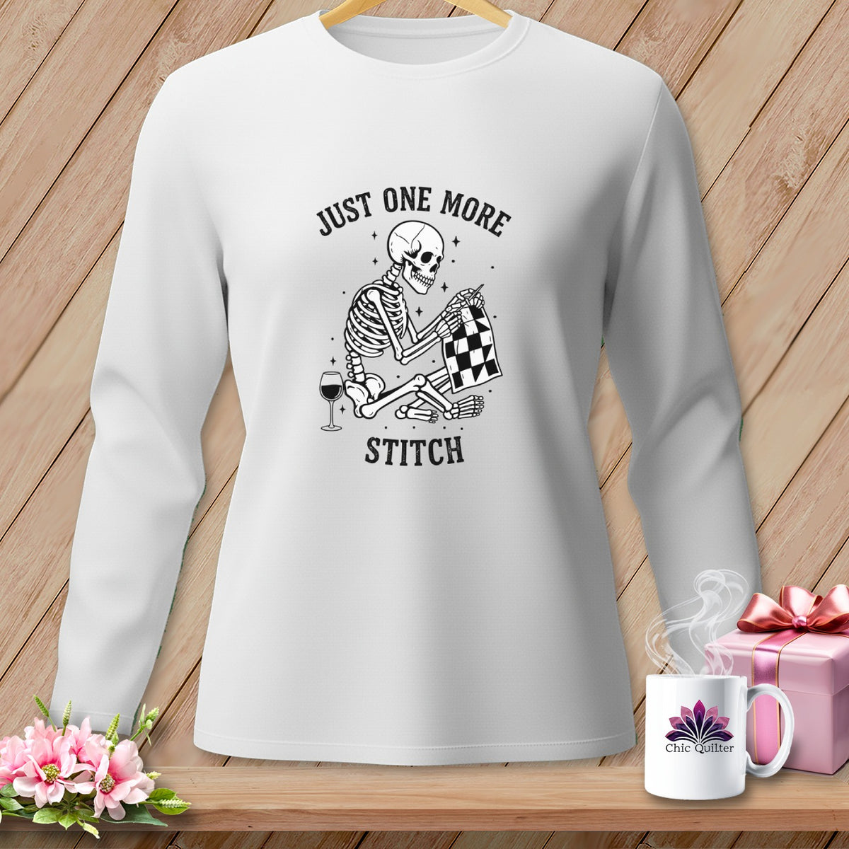 Skeleton sewing with wine and text "JUST ONE MORE STITCH" on shirt.