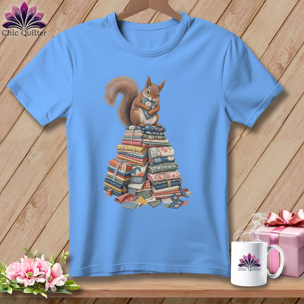 Light blue t-shirt with a squirrel hugging a fabric heart on a stack of quilts.