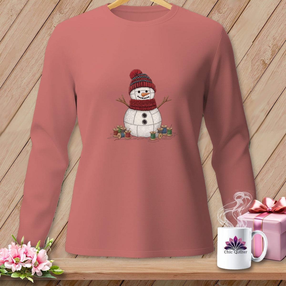 Pink long-sleeve shirt with a fabric snowman design, spools of thread, and a mug with "Chic Quilter" logo.