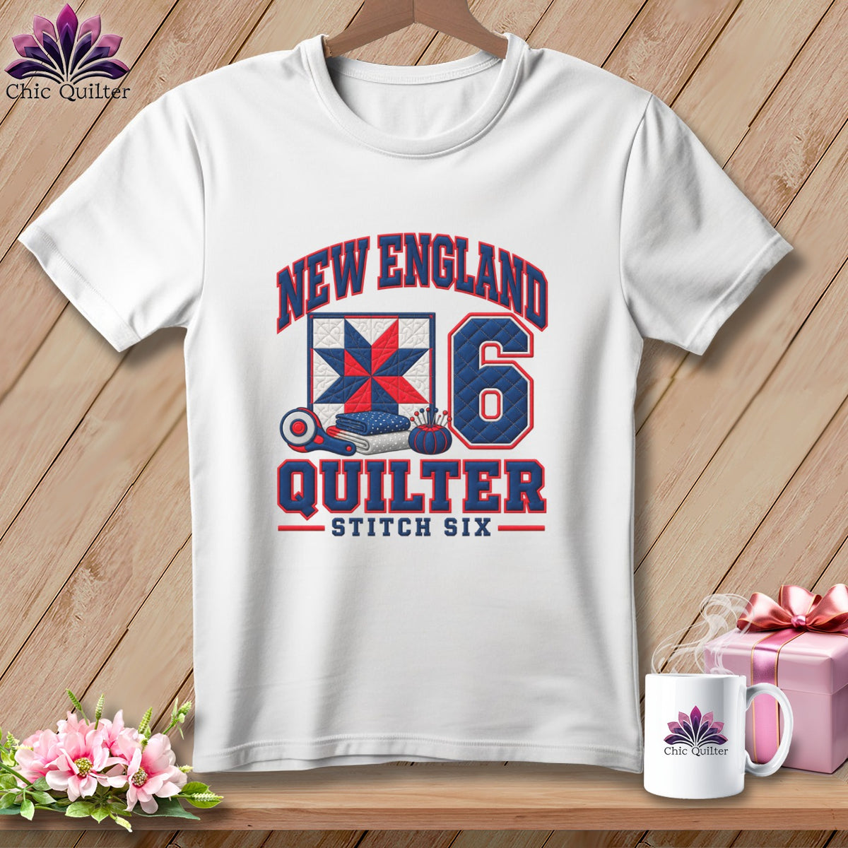 White short-sleeved t-shirt with a blue and red New England Quilter graphic on a wooden background.