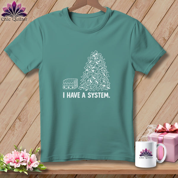 Teal t-shirt with a pile of fabric scraps and stacked fabric labeled "I HAVE A SYSTEM."